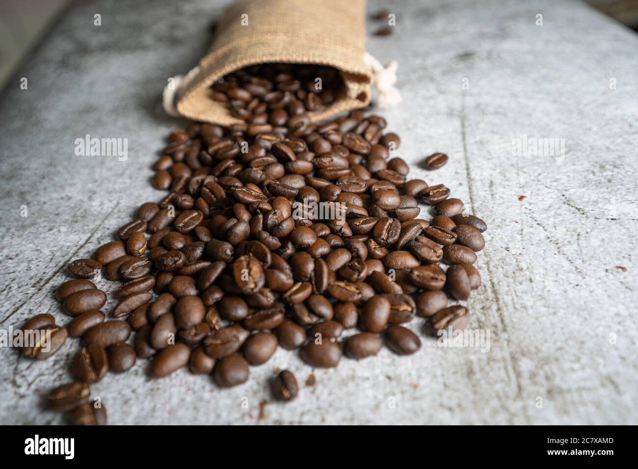 Roasted Arabica Coffee beans spread out on a table with a hessian sack in the background. The