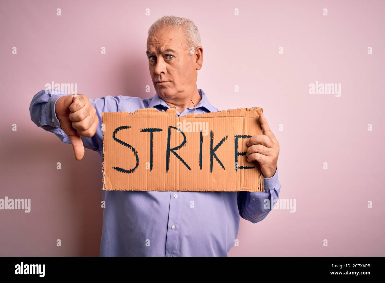 Middle age man asking for rights holding banner with strike message over pink background with angry face, negative sign showing dislike with thumbs do Stock Photo