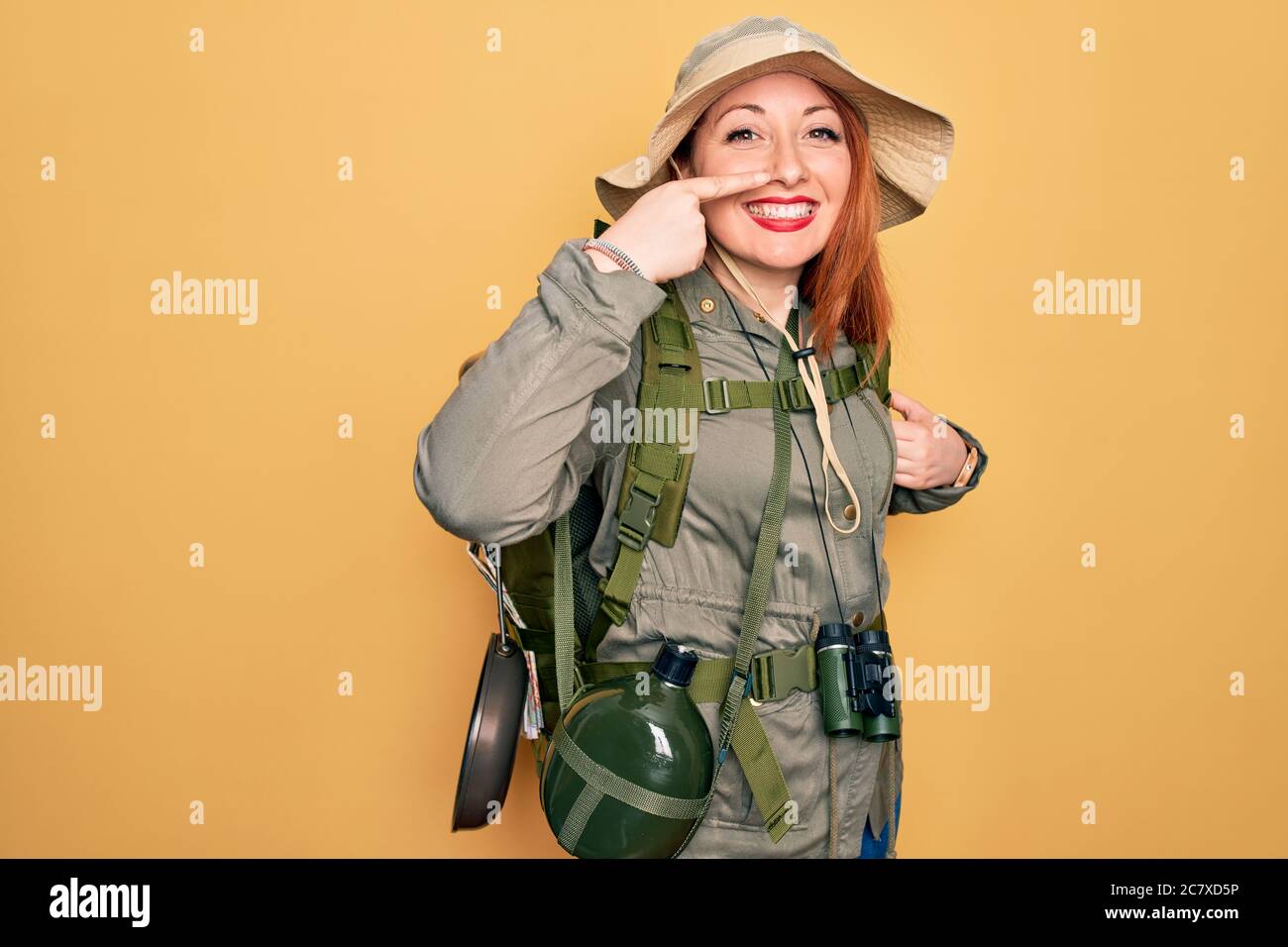 Young redhead backpacker woman hiking wearing backpack and hat over ...