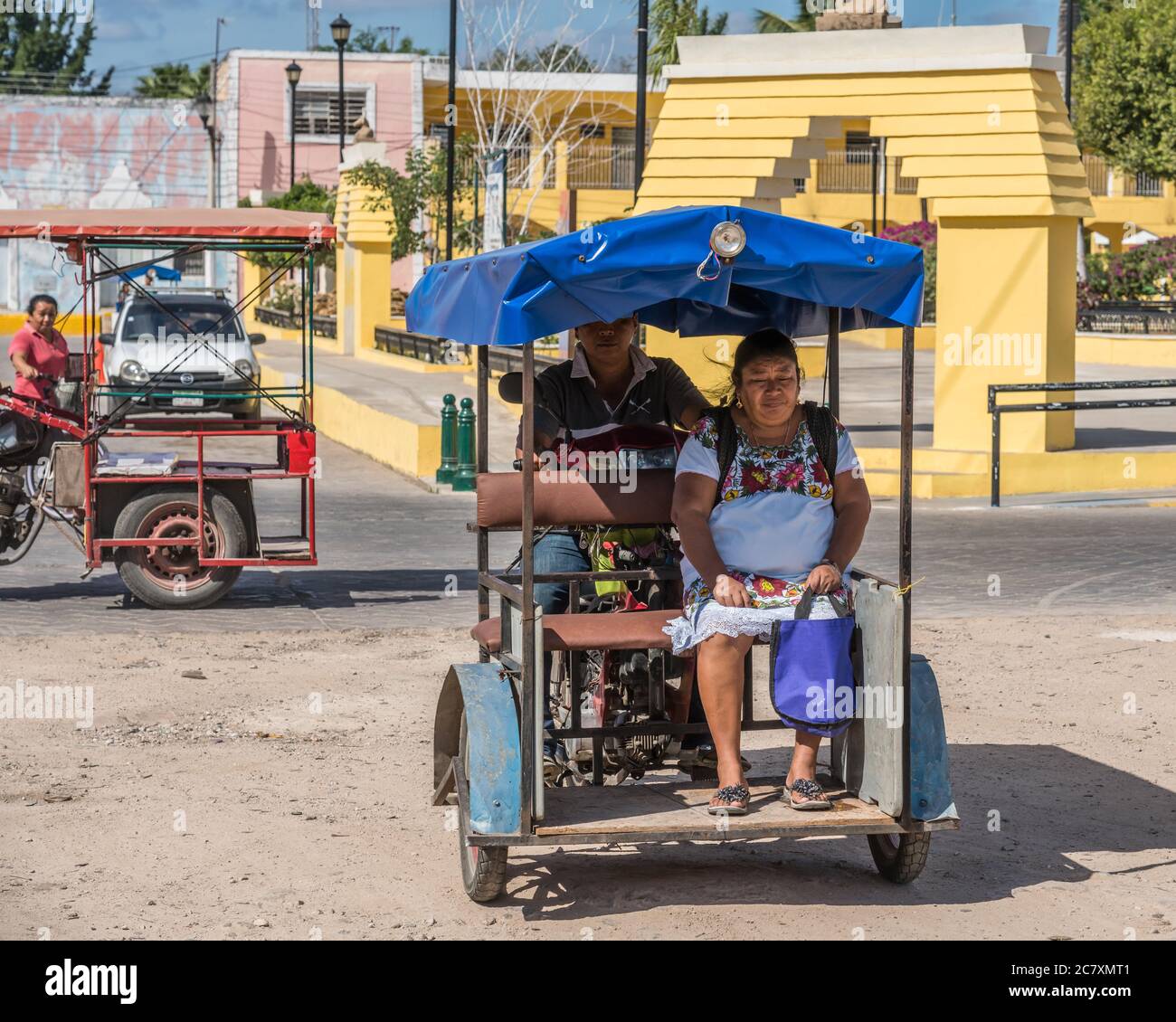 An indigenous Mayan woman in a traditional embroidered huipil in a motorcycle taxi in front of the market in Acanceh, Yucatan, Mexico. Stock Photo