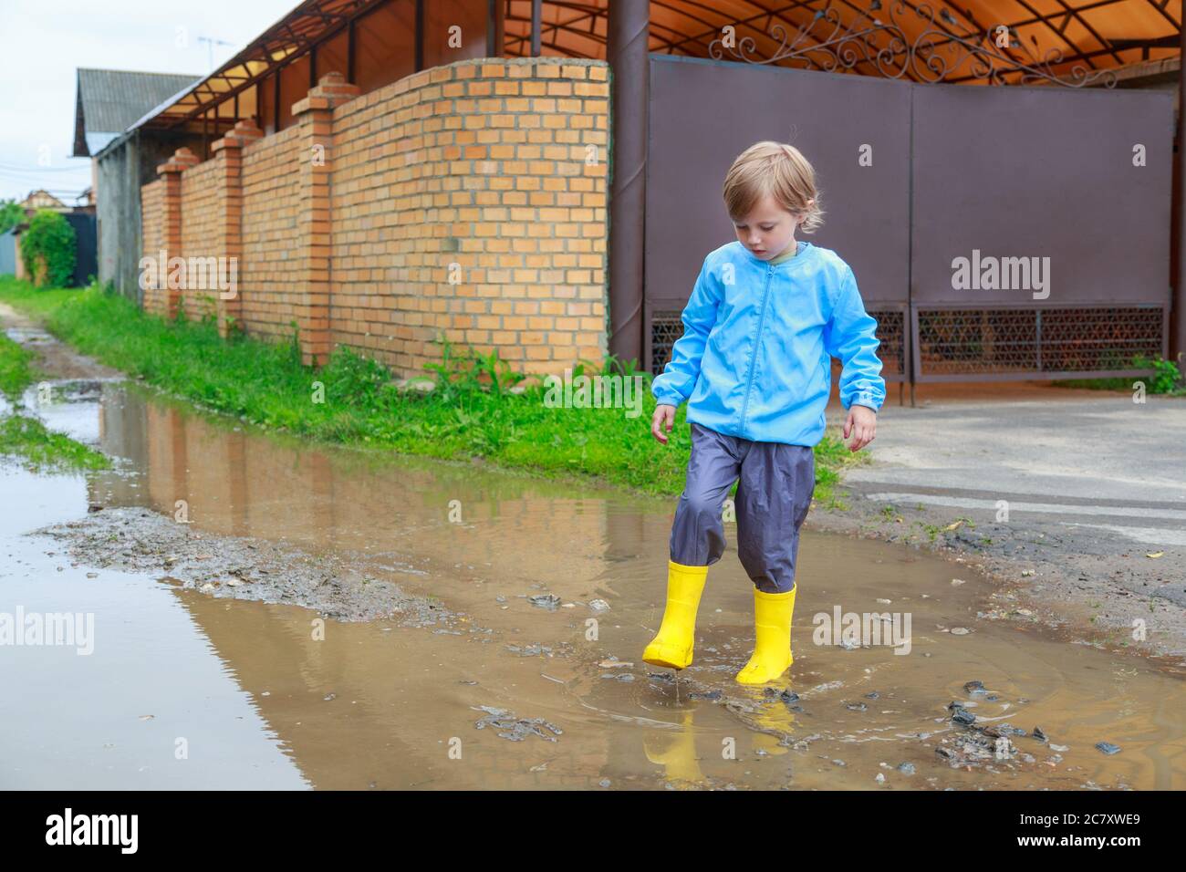 .Child in rubber boots and raincoat playing in a puddle Stock Photo - Alamy