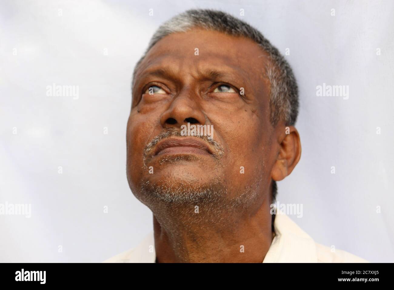 Closed mouth and beard of a senior Indian man looking up, white background. Old Indian man with black and white hair. Stock Photo