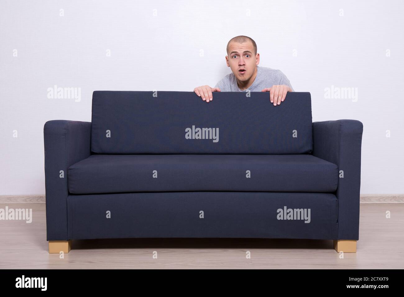 young man hiding behind a sofa at home Stock Photo Alamy
