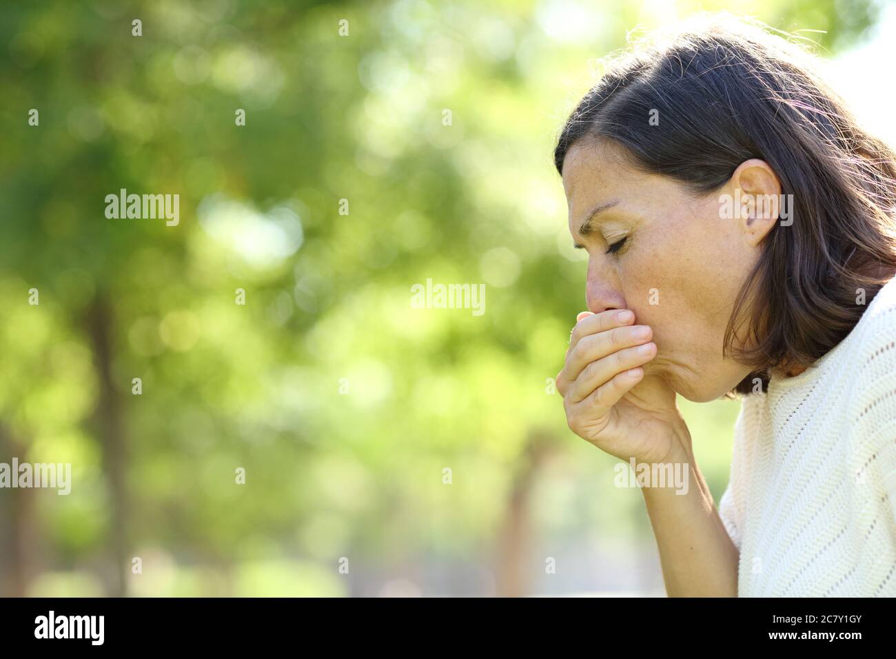 Sick adult woman coughing standing in the park at summer Stock Photo