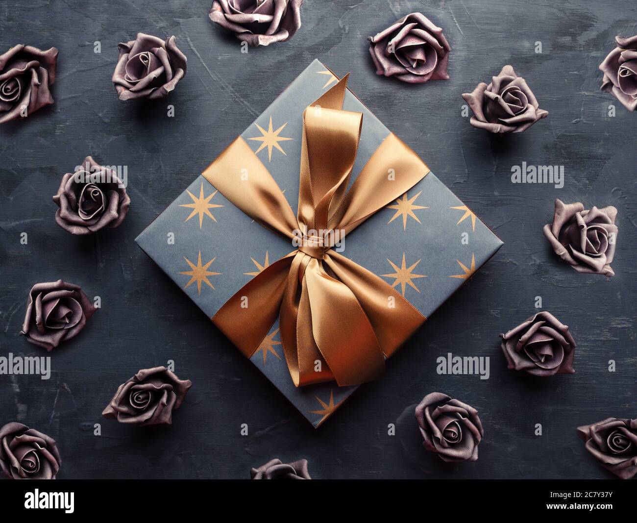 Blue gift box with gold ribbon bow and artificial violet roses on blue ...