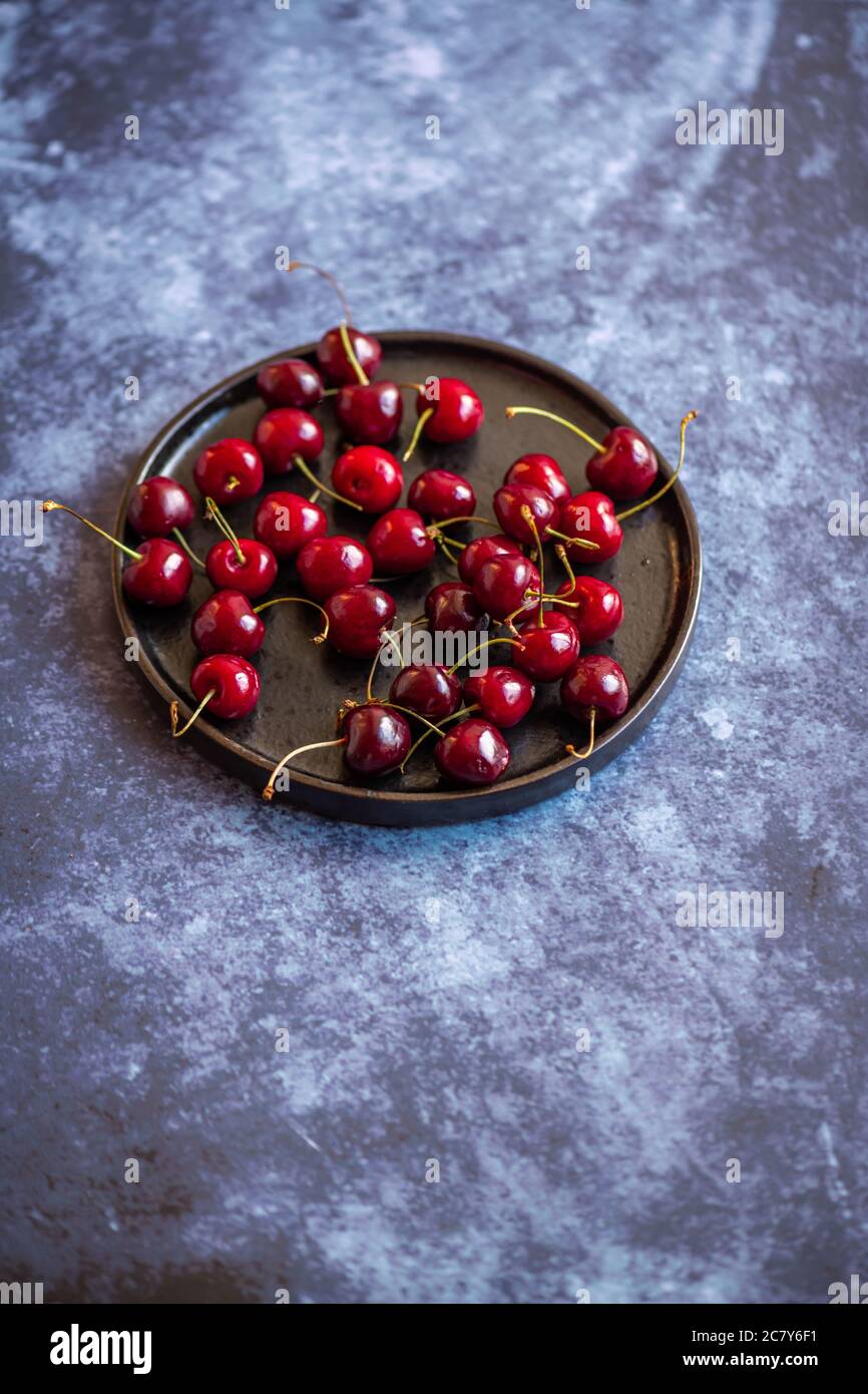 Vertical image of red ripe cherries on a saucer on a concrete surface ...