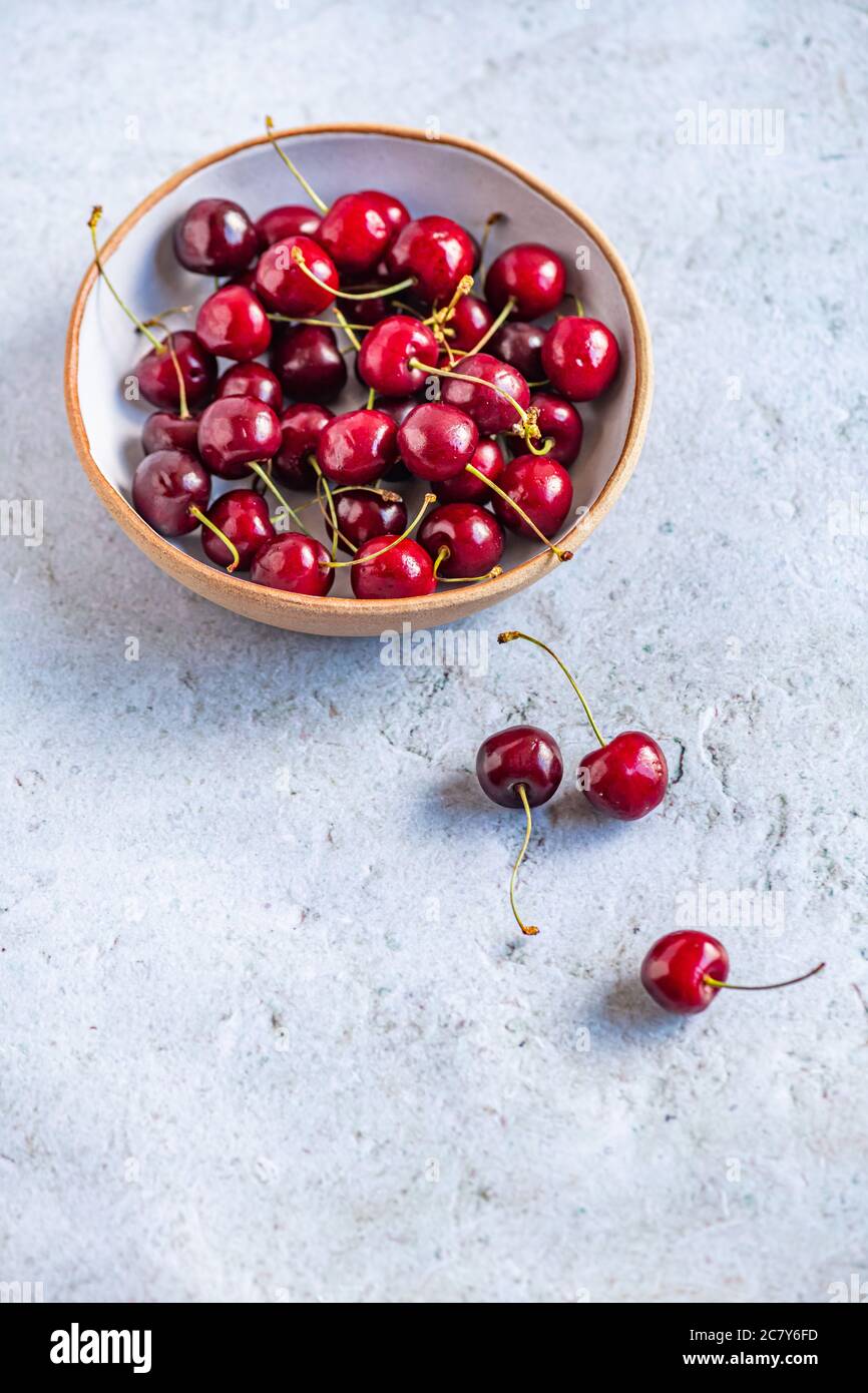 Vertical image of red ripe cherries in a bowl on a concrete surface ...