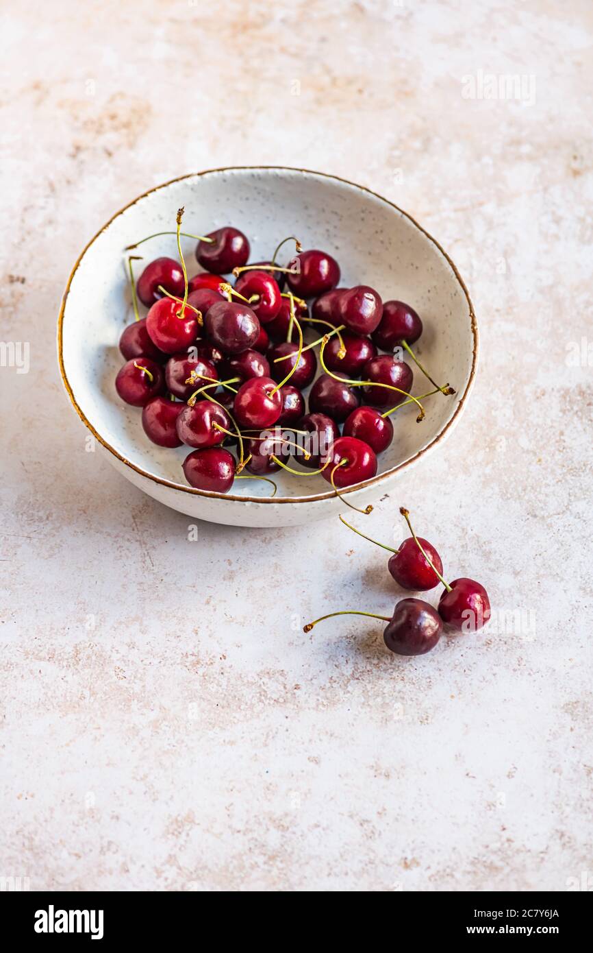 Vertical image of red ripe cherries in a bowl on a concrete surface ...