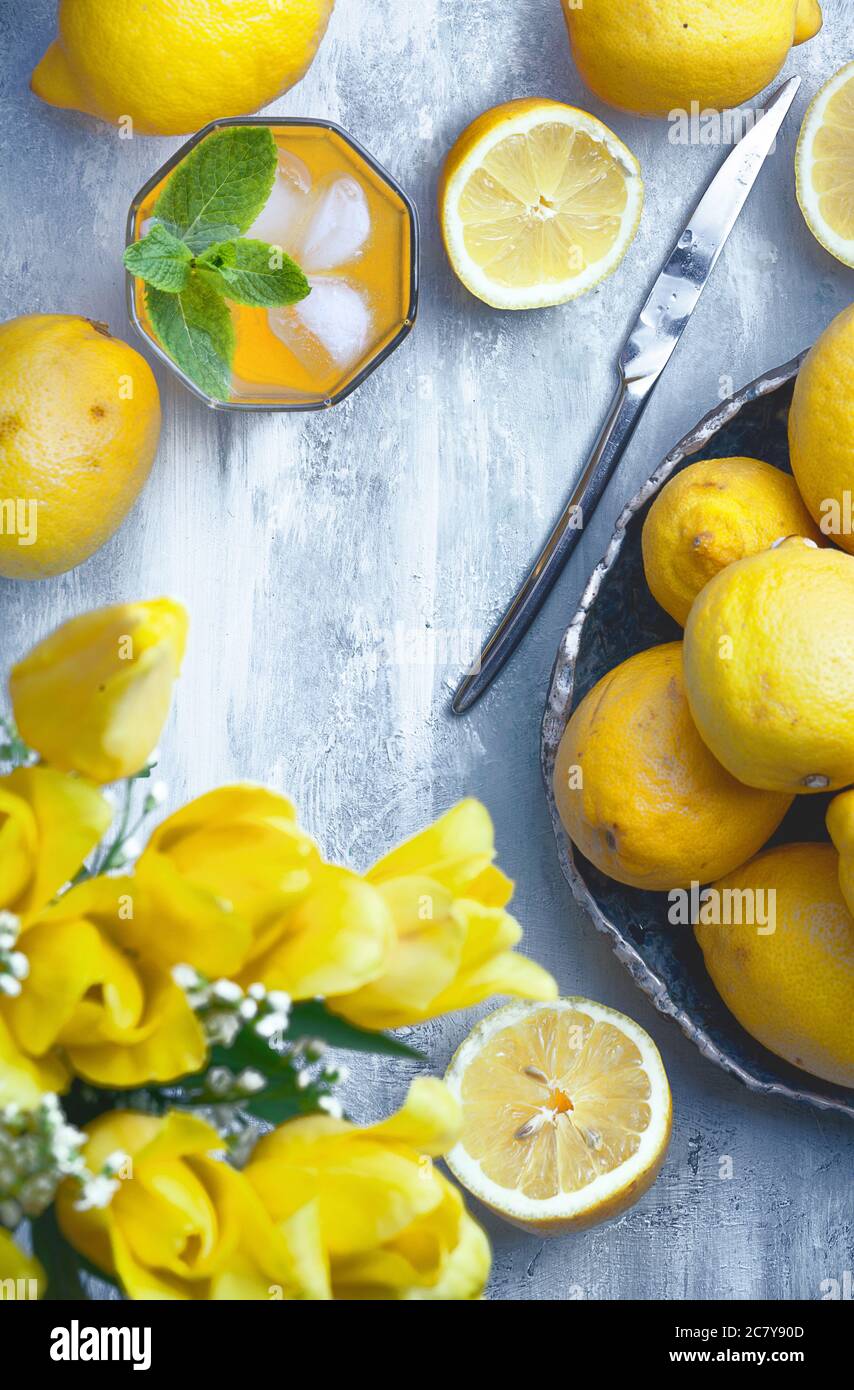 bright flatlay food background - empty wooden board with lots of lemons, glass of lemon juice, yellow flowers and knife, with copy space for text Stock Photo