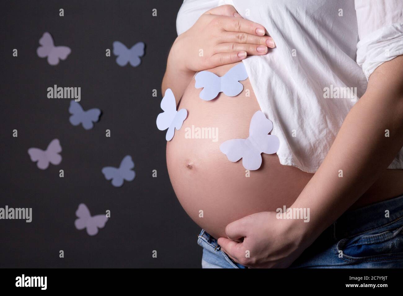 pregnant woman's belly with colorful butterflies over grey background