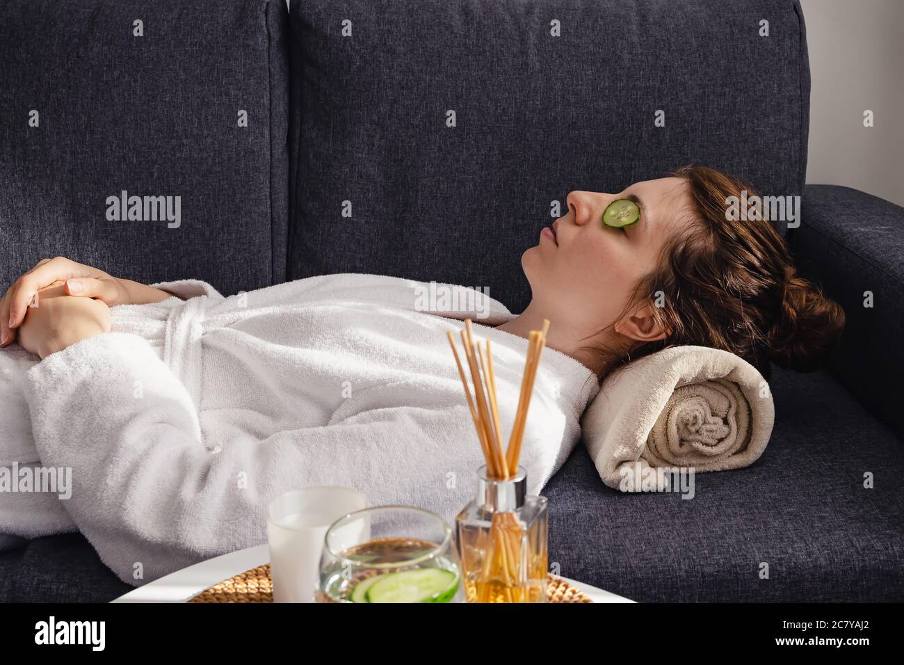 Young relaxing woman in bathrobe applying cucumbers on eyes at home. Self care routine, wellbeing Stock Photo