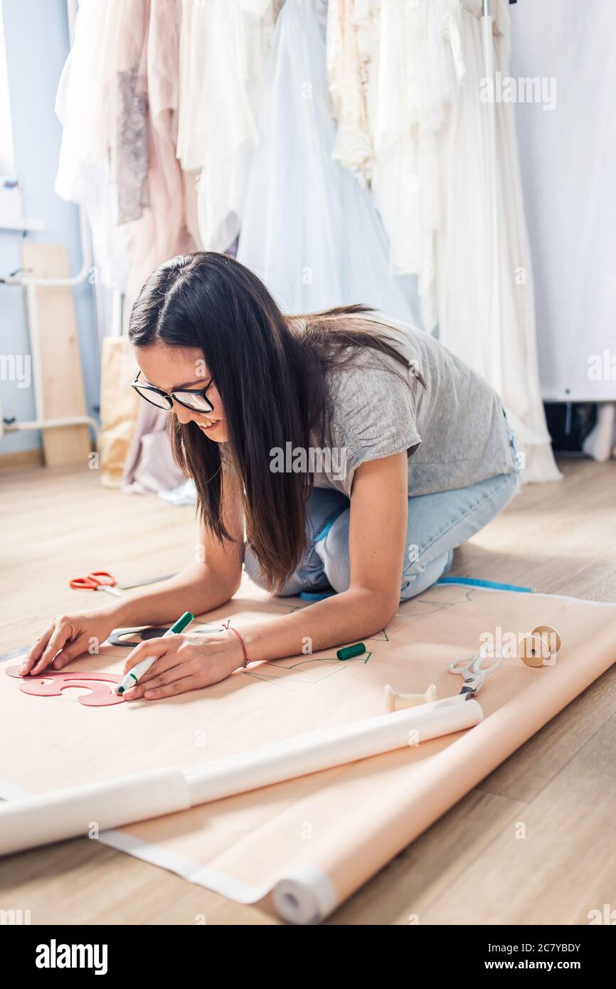 Focused attractive young woman tailor standing and drawing on textile ...