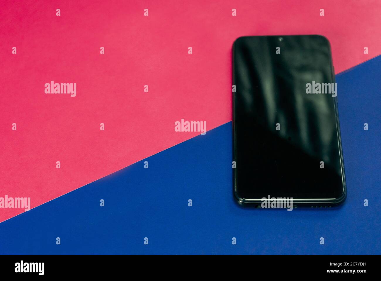 Closeup shot of a black smartphone on a blue and pink triangular ...