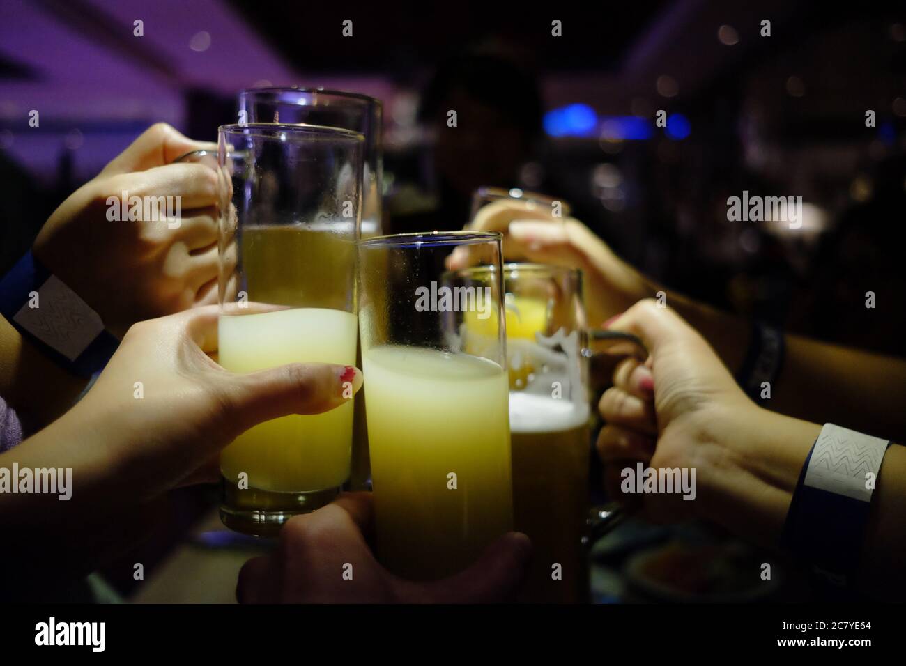 cheers! close up several hands raise glasses with juice and wine, cheering under bar light in party. dark blur background. cooperation teamwork concep Stock Photo