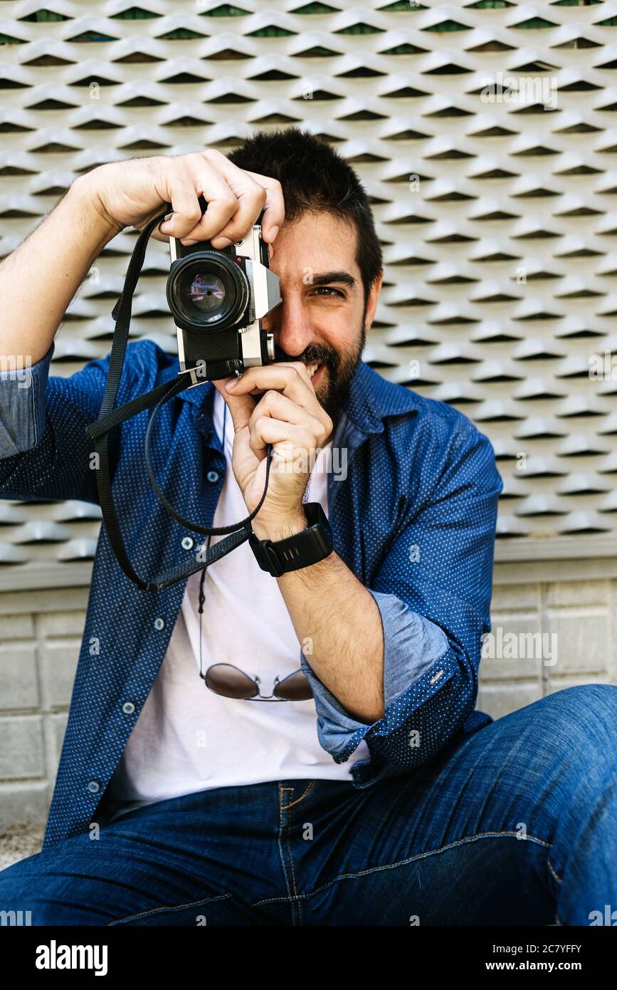 Cheerful bearded traveler man sitting on ground while using checking a camera Stock Photo