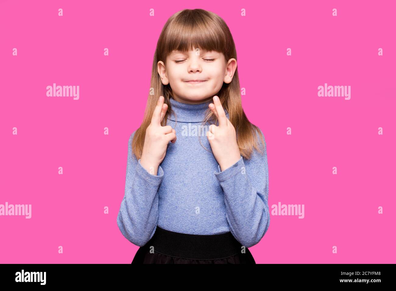 Funny little girl crossing fingers, hoping her wish come true, isolated on pink background. Portrait of small girl praying, wishing good luck or mirac Stock Photo