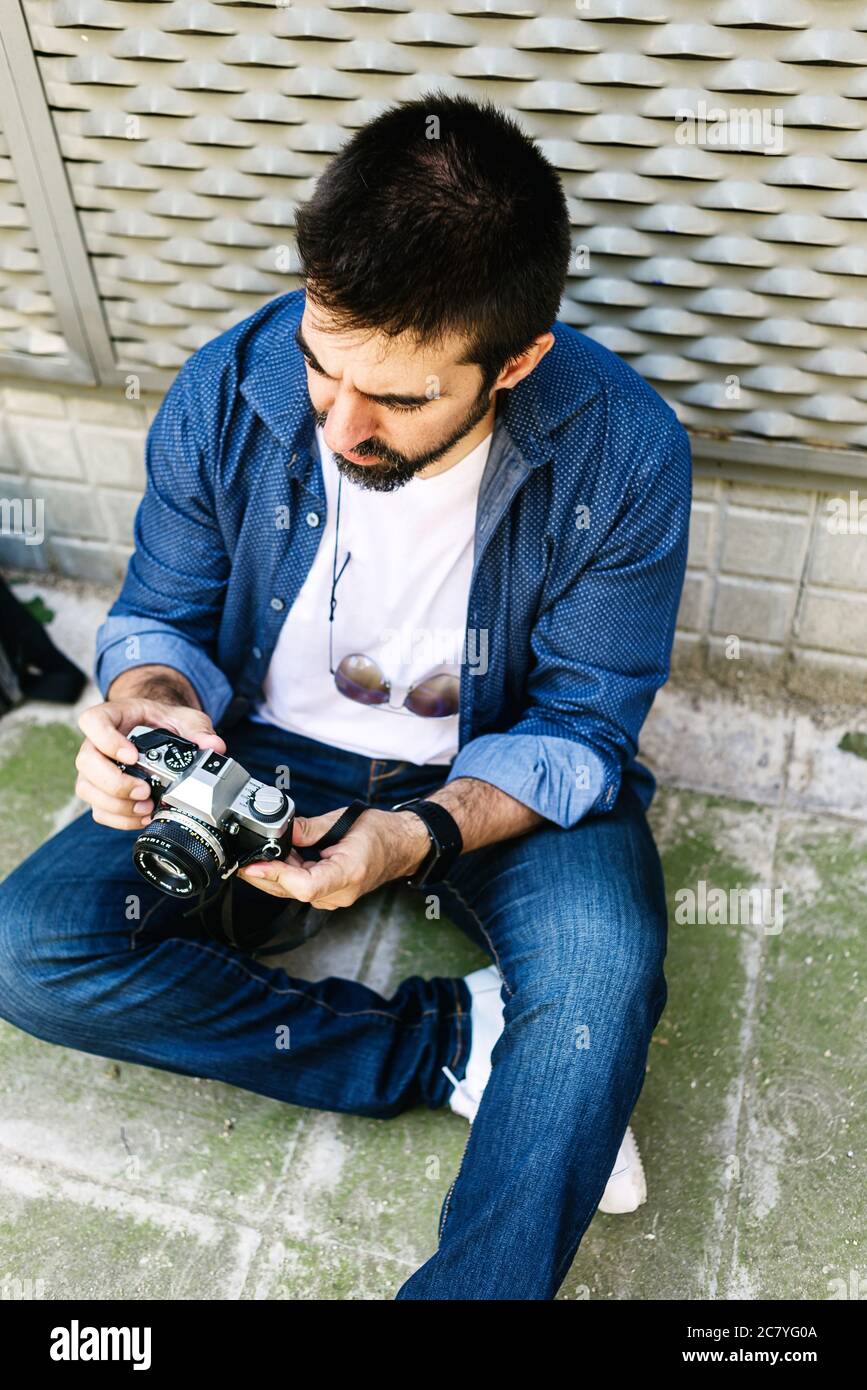 Cheerful bearded traveler man sitting on ground while using checking a camera Stock Photo