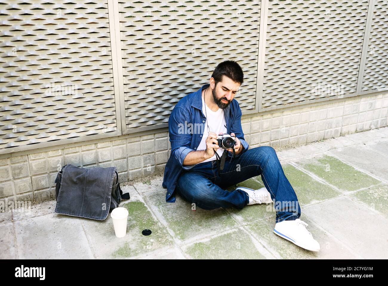 Cheerful bearded traveler man sitting on ground while using checking a camera Stock Photo