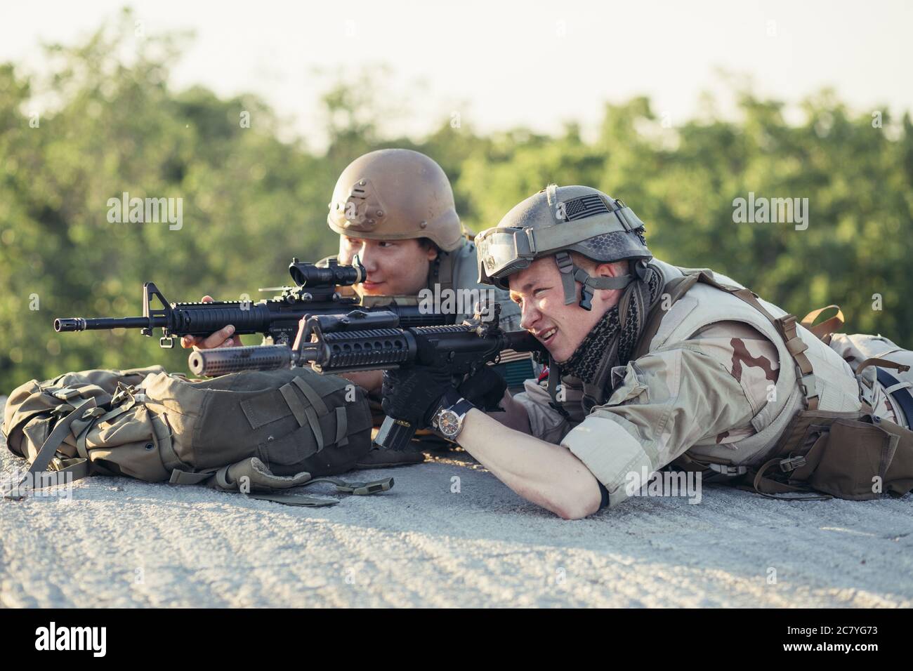 Pair of Army Rangers with rifle and machine gun moving along the concrete wall on mission. They are ready to start firing if enemy appear. Outdoor loc Stock Photo