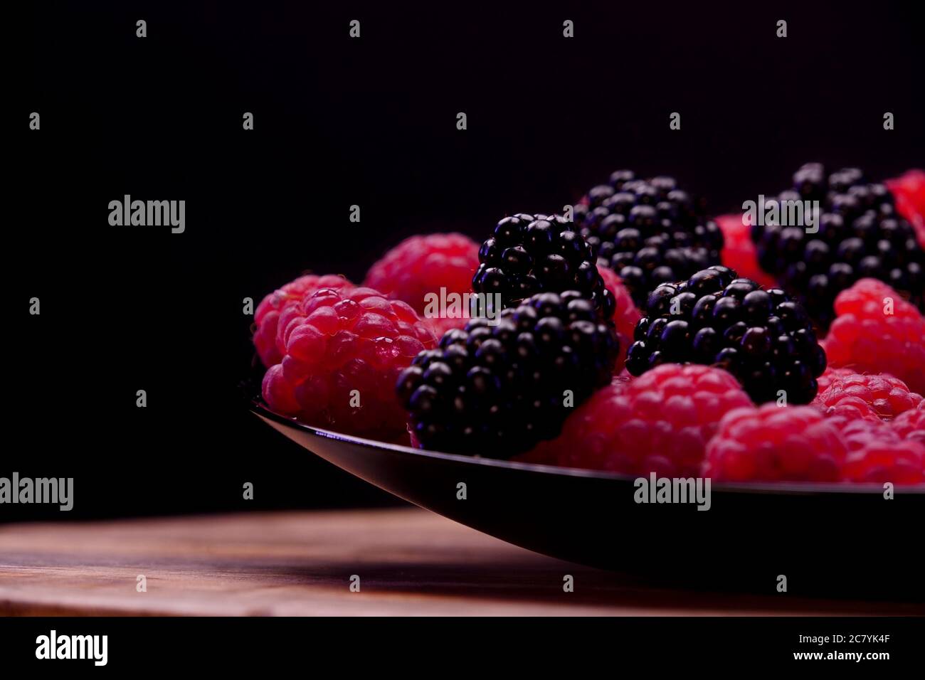 Blackberries and raspberries fruits composition on a black plate and black background. Fresh and tasty looking organic food for vegan in a summer seas Stock Photo