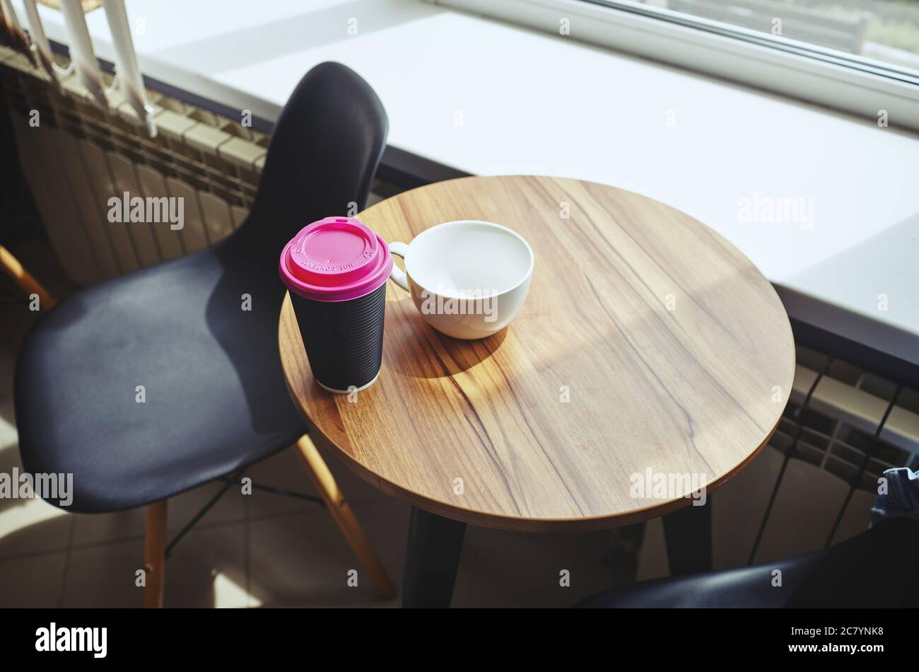 Disposable coffee paper cup and empty white mug on table in cafe