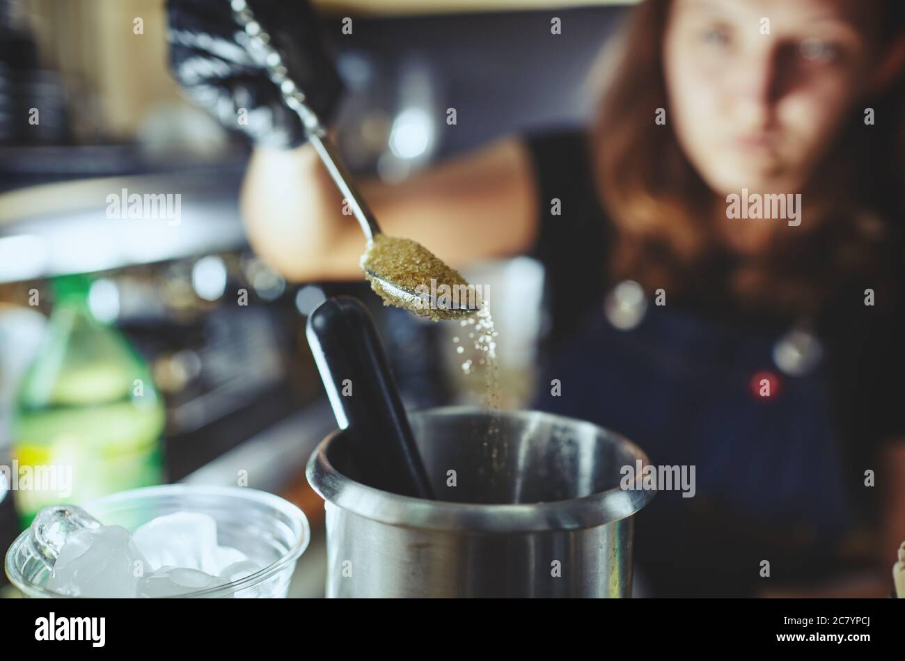 Bartender wearing medical latex black gloves,making mojito cocktail.Process of bartending in bar,pouring a tablespoon of brown sugar in shaker Stock Photo