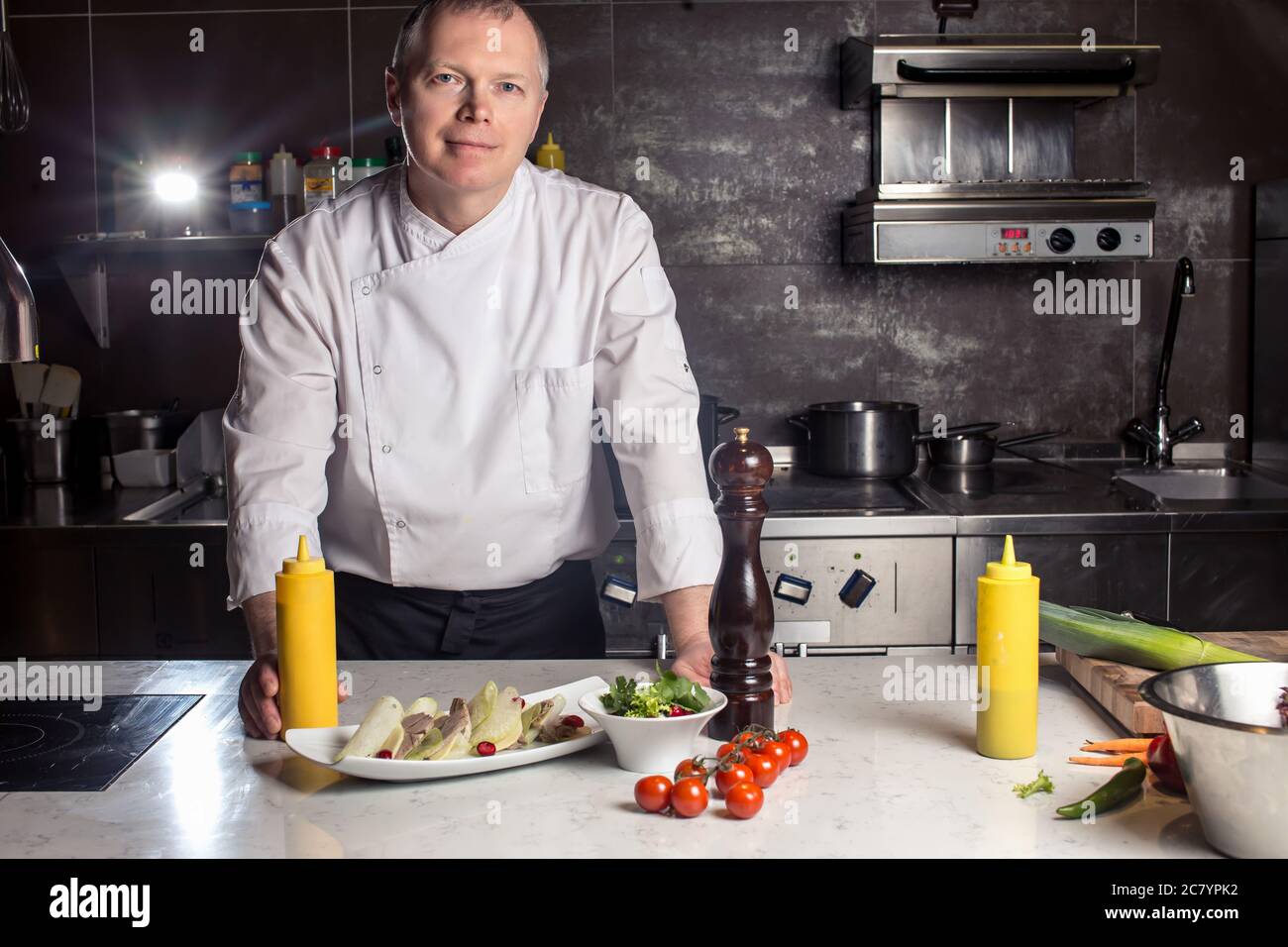 Chef leaning on the counter with a dish in a commercial kitchen Stock ...