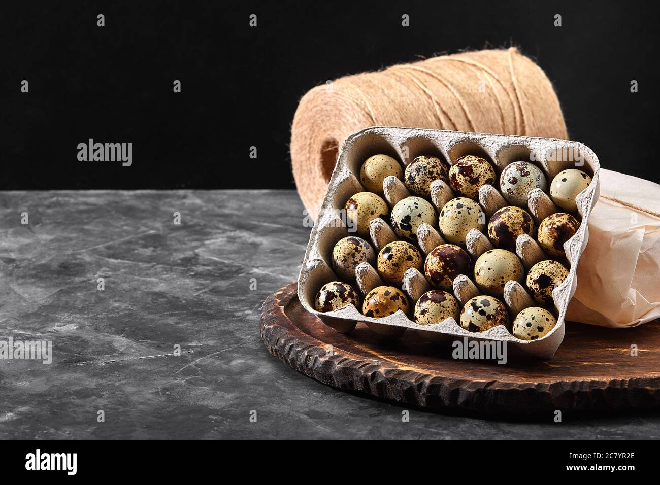 Quail eggs in a gray cardboard box. Closeup photo. Black concrete