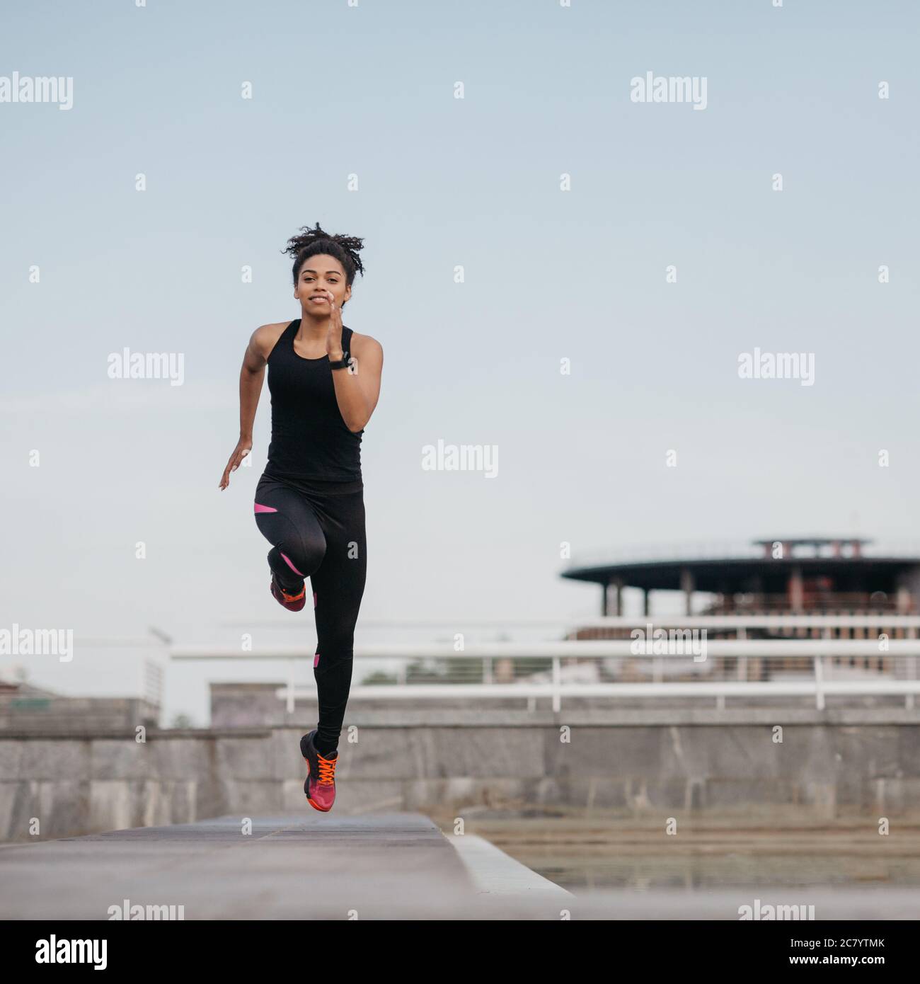 Running with jumps in training. African american girl in sport uniform in jump, on stadium Stock Photo