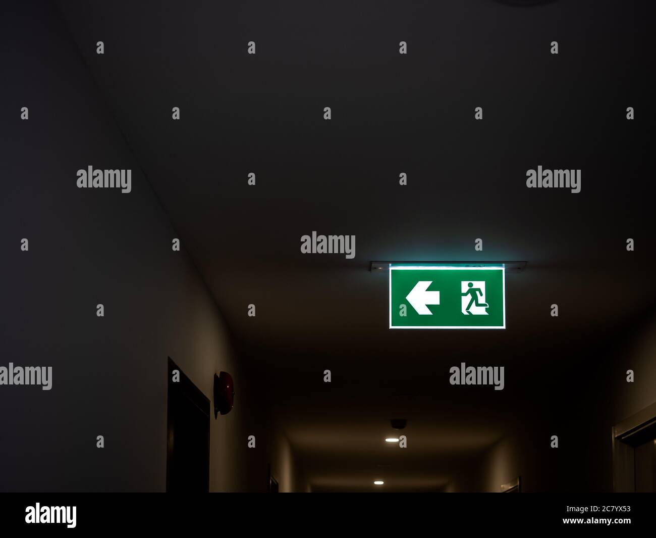 Fire exit. Illuminated green emergency exit sign hanging on ceiling in