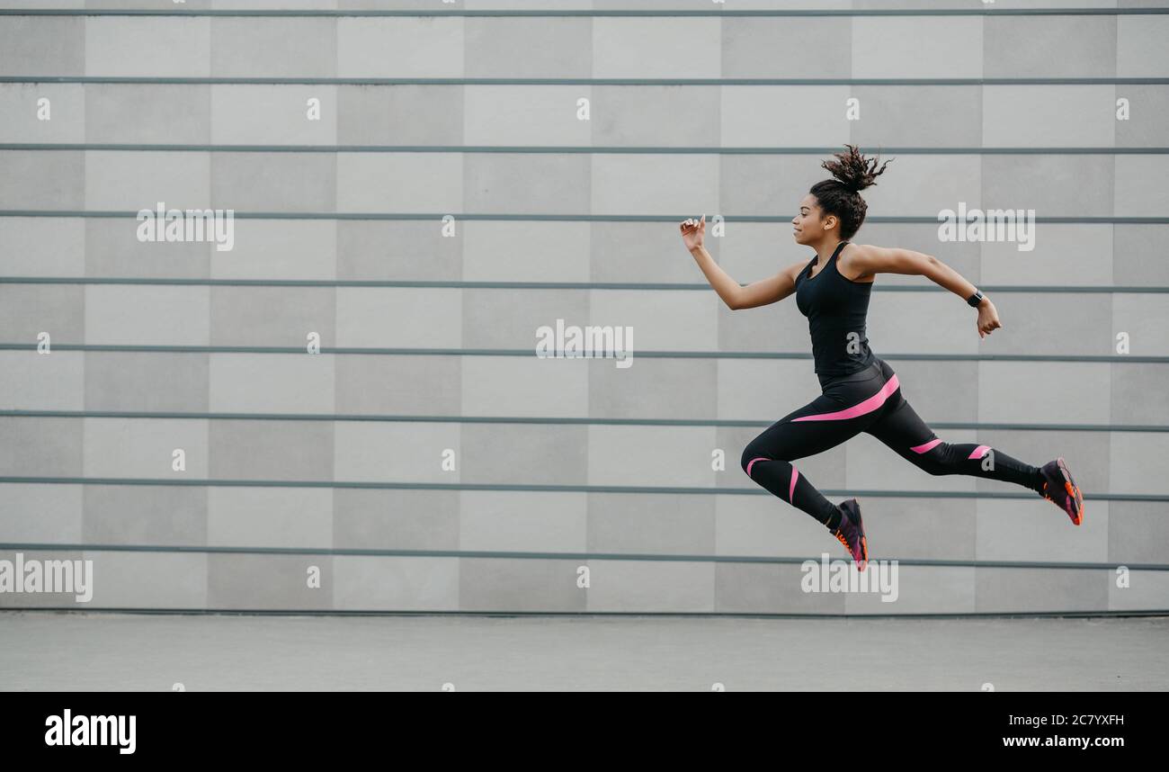 Excellent training running. African american girl in sportswear froze in air above ground, jumping Stock Photo