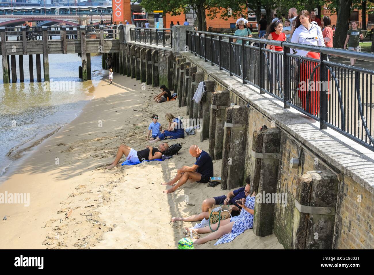 People sunbathe on the sandy beach bank of the River Thames, South Bank, London, England, UK Stock Photo