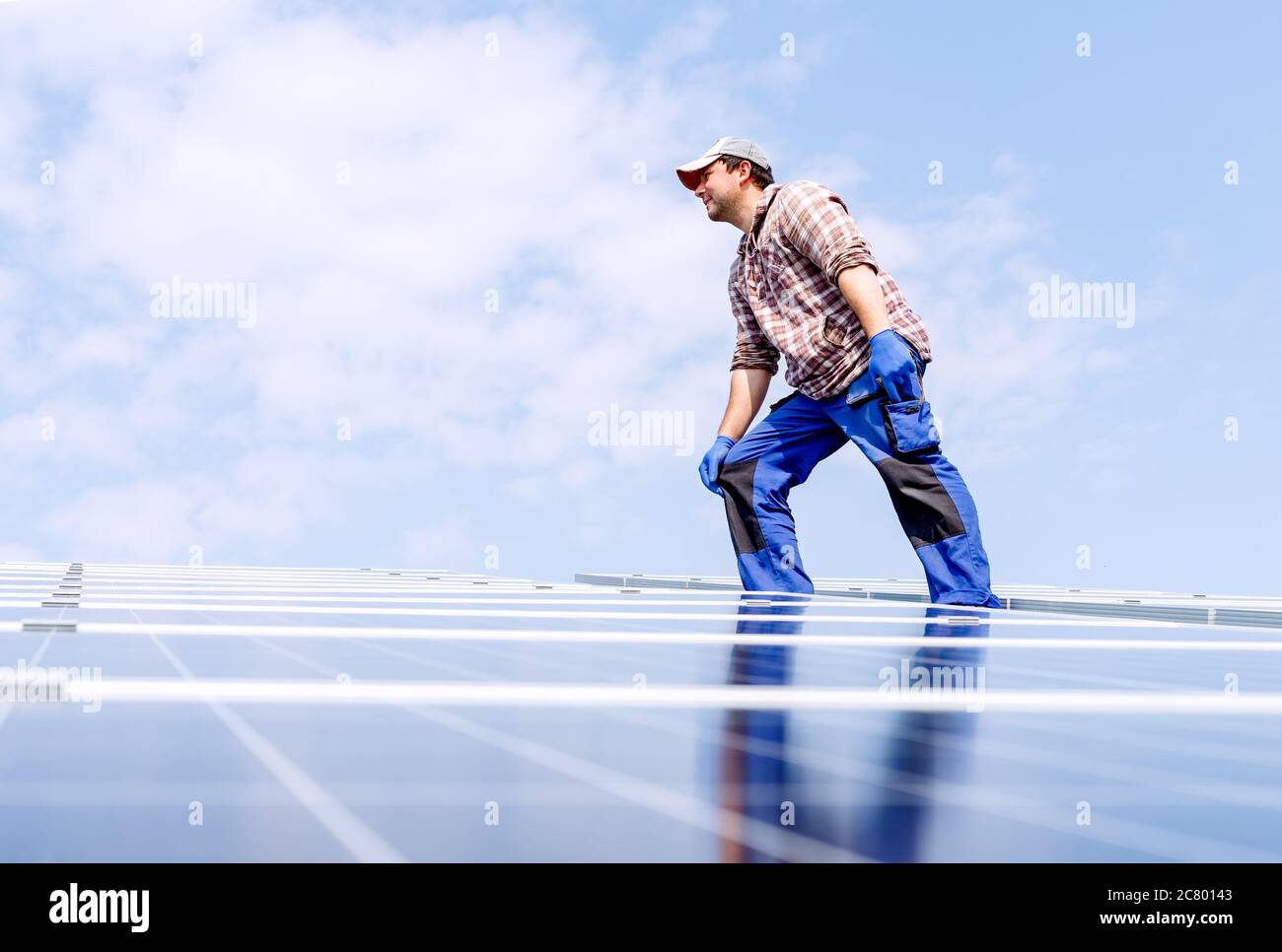 Solar panel energy. Electrical engineer man is working in solar station on roof against blue sky in sunny day. Development sun alternative energy Stock Photo