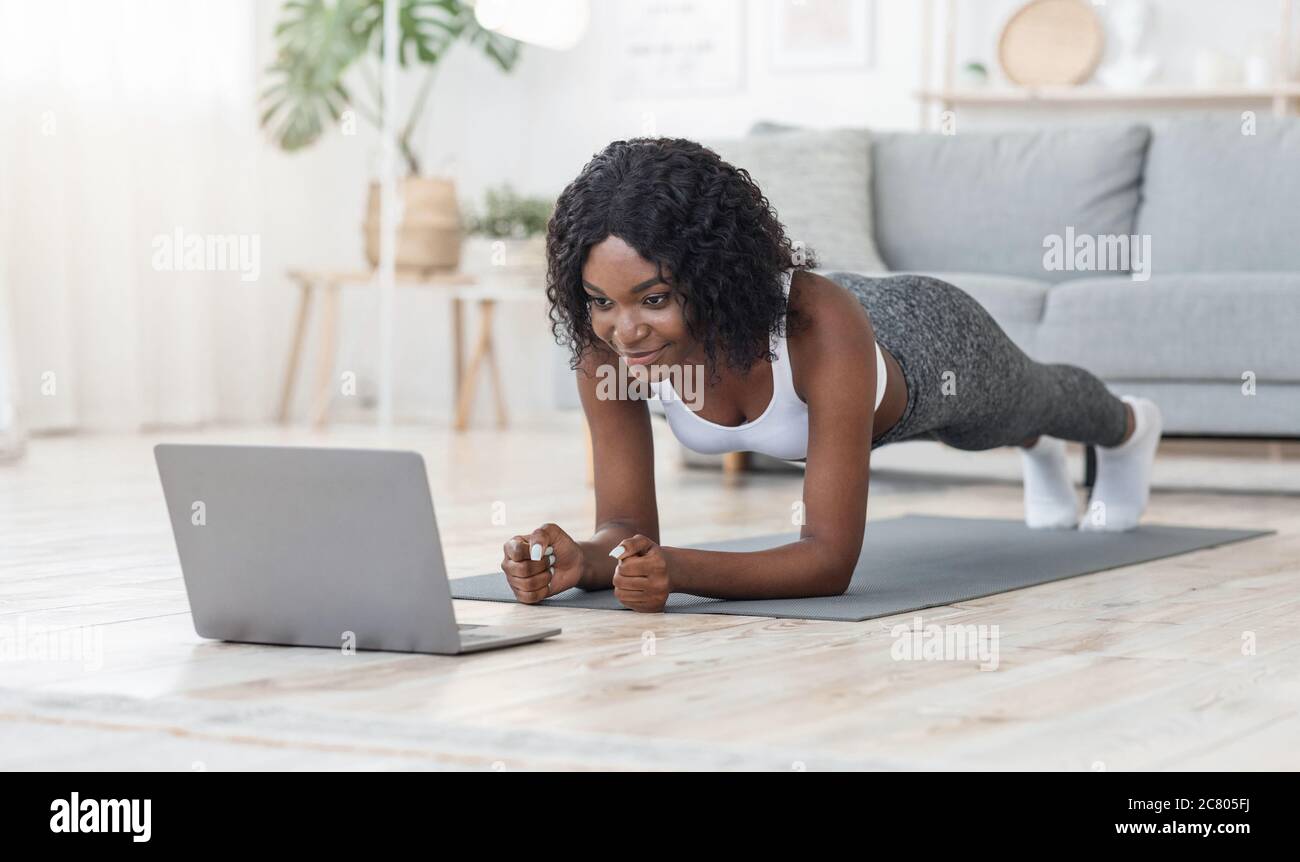 Black girl planking at living room, looking at laptop screen Stock Photo