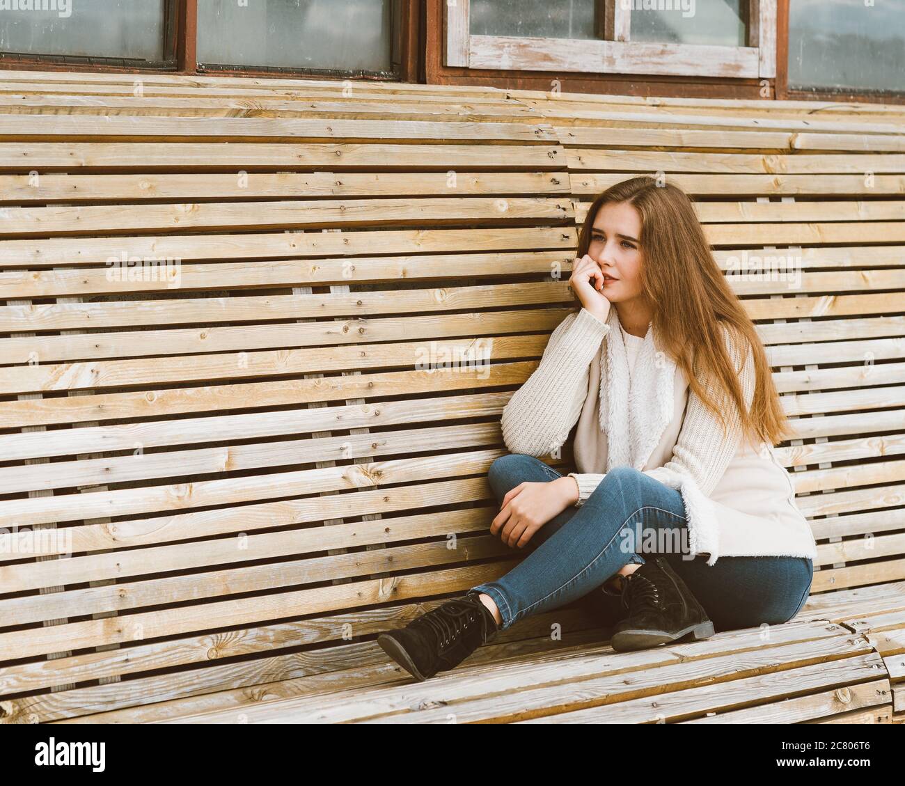 Beautiful young girl with long brown hair sits on wooden bench made of ...