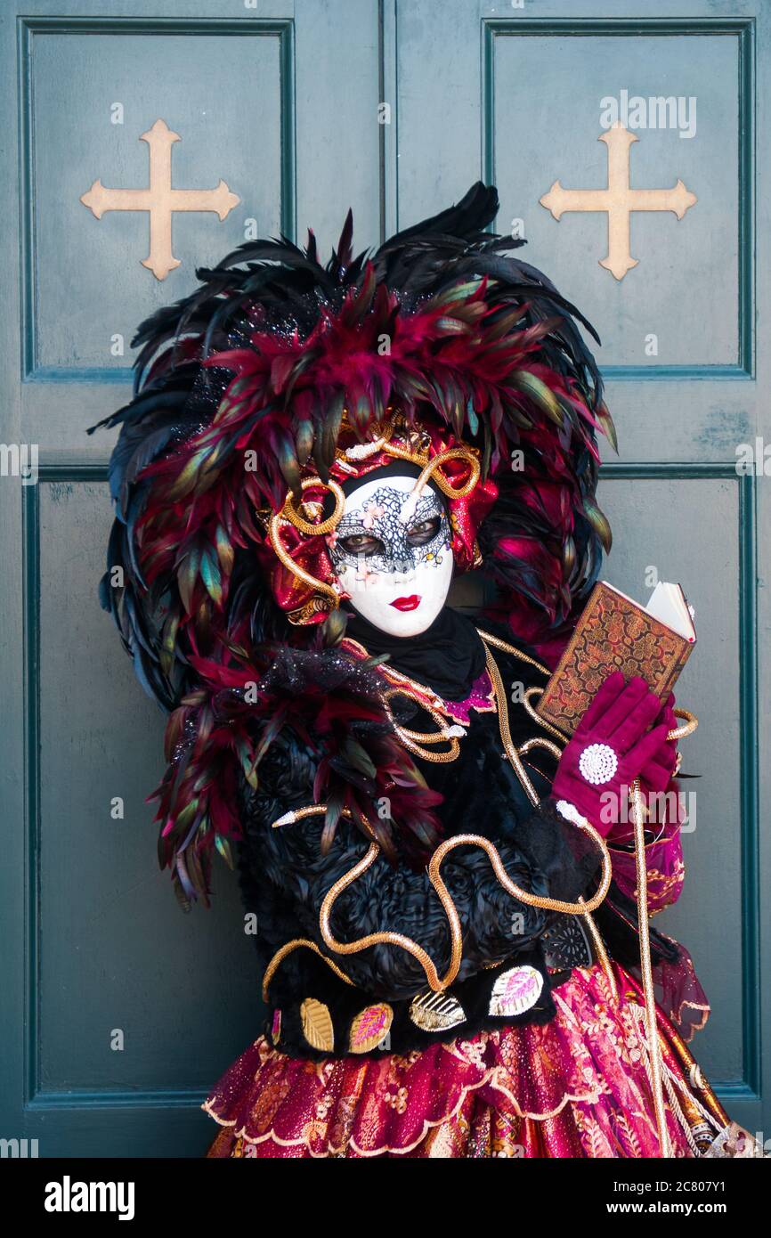 A dame costume with black and red feathers poses with a book in her hand Stock Photo