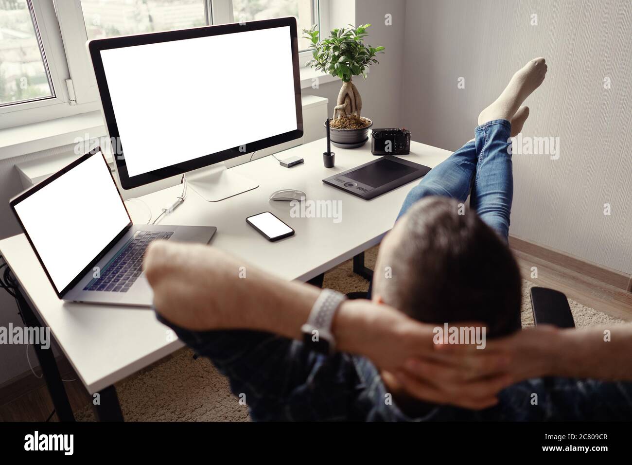 Man relaxing while working remotely from home holding legs on the table  looking at the laptop, monitor and phone blank display Stock Photo - Alamy