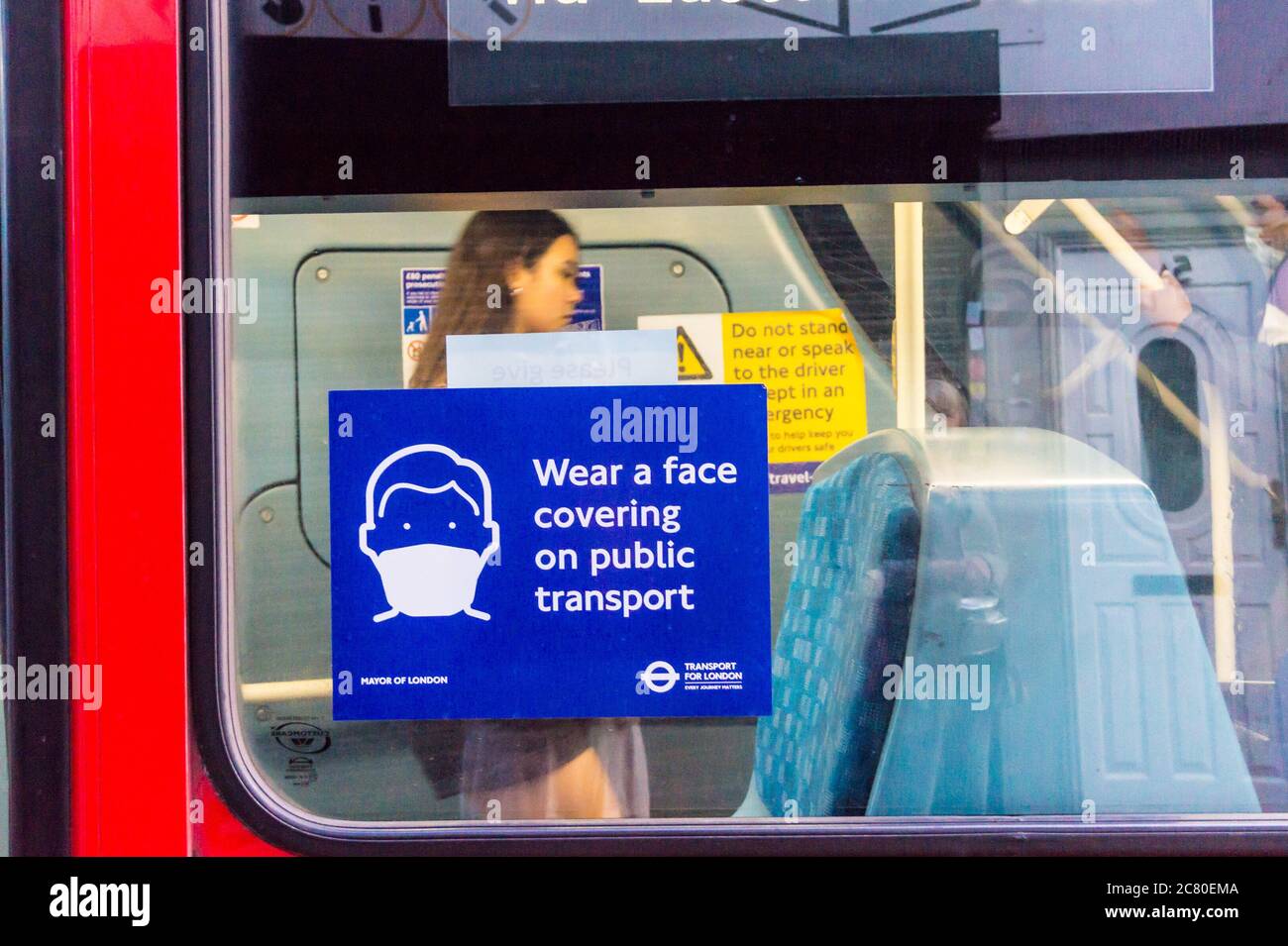 Face covering sign on a London bus with a young woman inside without a mask. Image taken before wearing a covering was required by law. Stock Photo