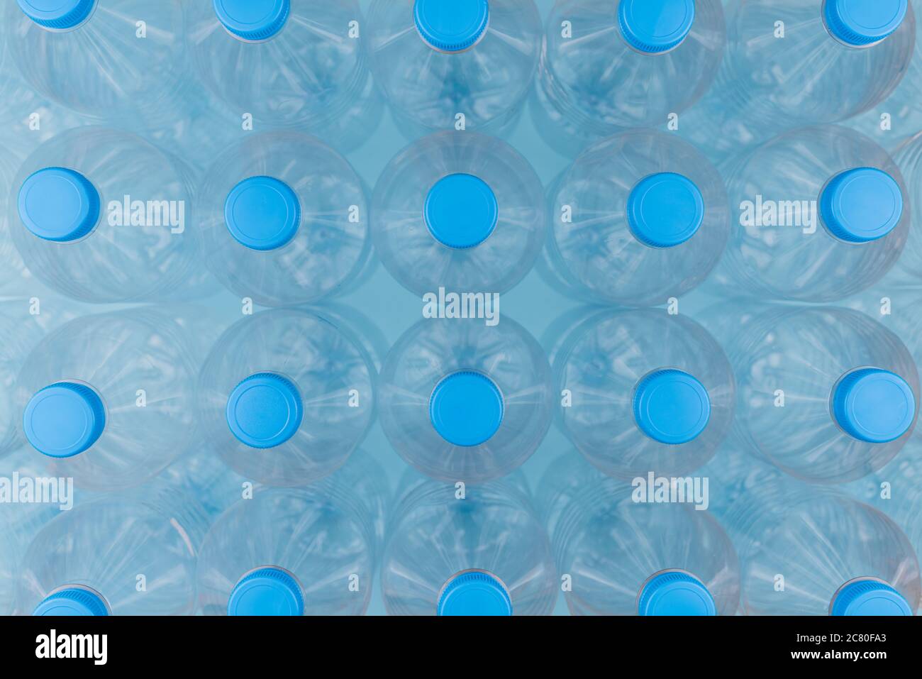 Horizontal color image with an overhead view of an empty clear plastic bottles with caps stacked on a blue background. Recycling and environment conce Stock Photo