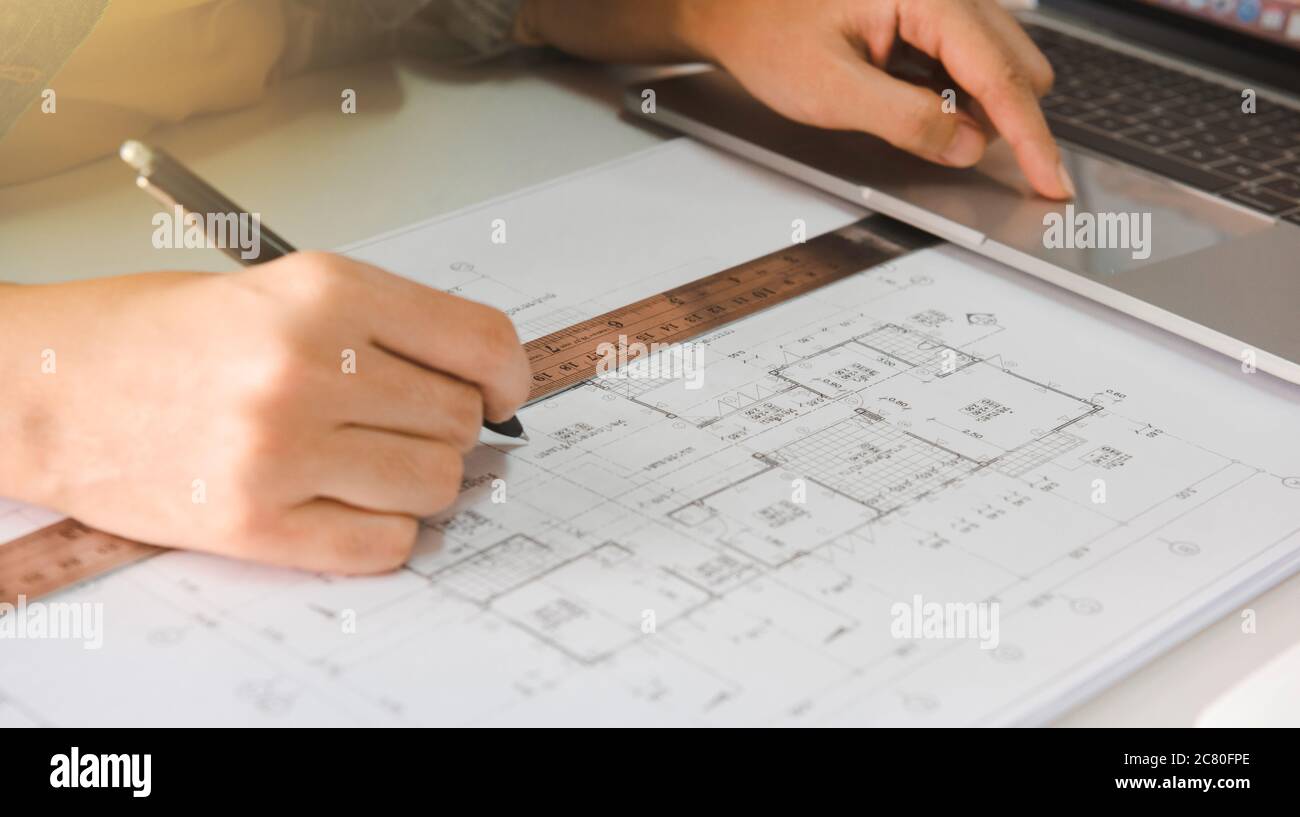 Engineers holding a pen pointing to a building and using laptop to planning project schedule. Engineering and construction concept. Stock Photo