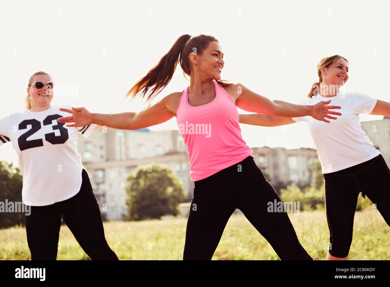 Group of happy young women fitness training doing a cardiovascular workout outdoors with arm stretches in an urban park Stock Photo