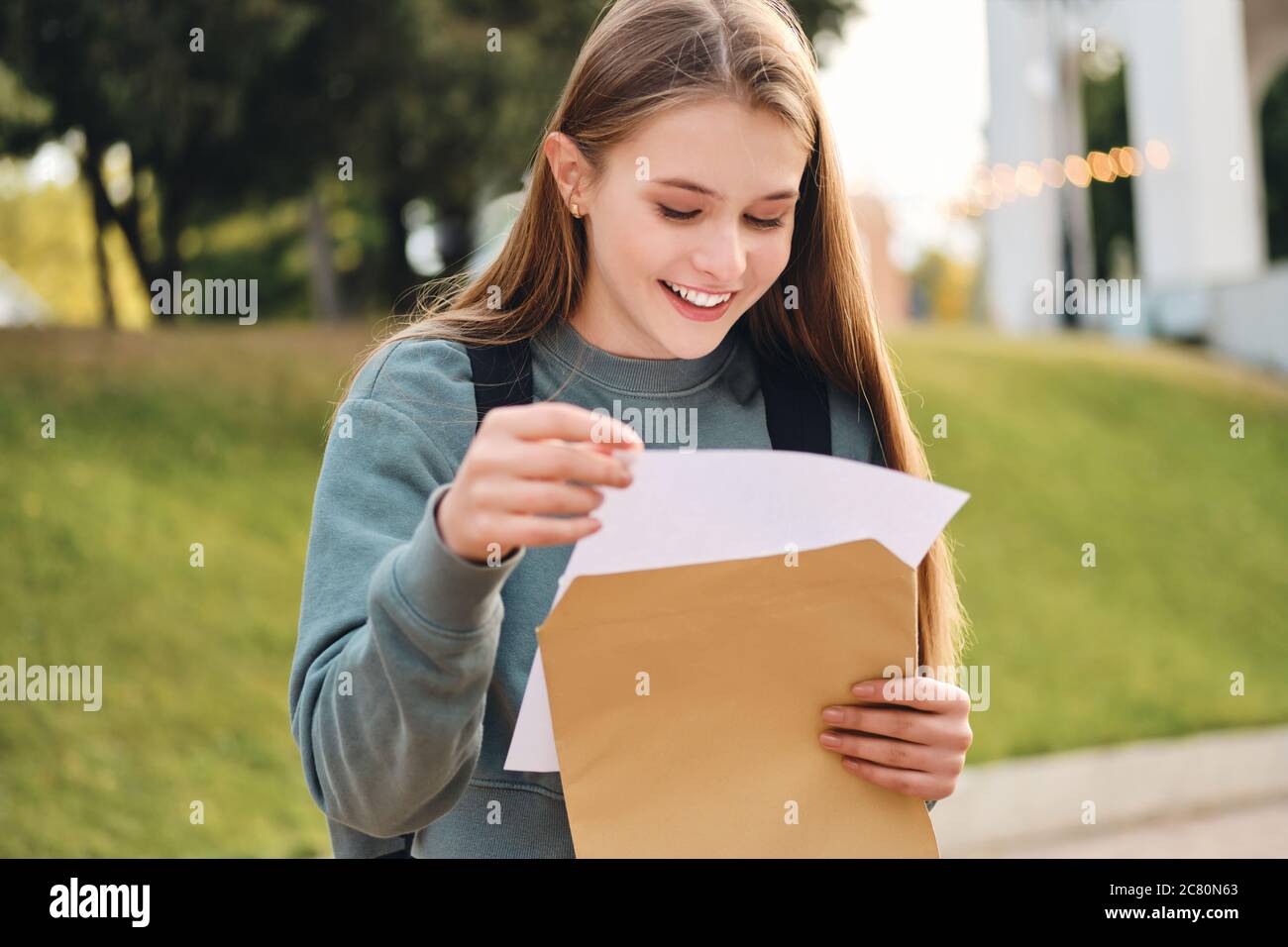 Attractive casual student girl joyfully opening envelope with exams results in park Stock Photo