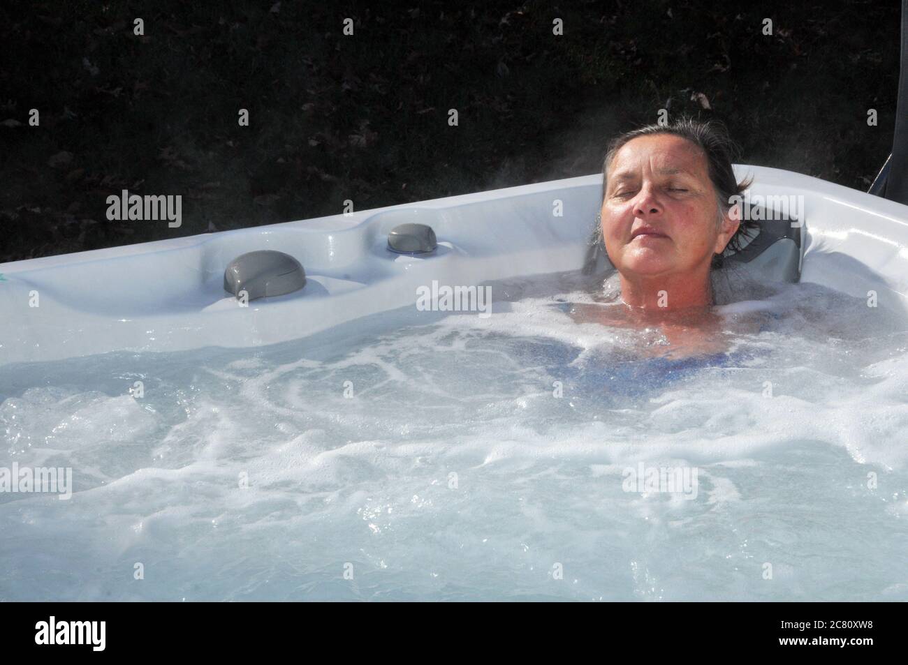 Middle aged woman relaxing with eyes closed in whirlpool hot tub Stock Photo