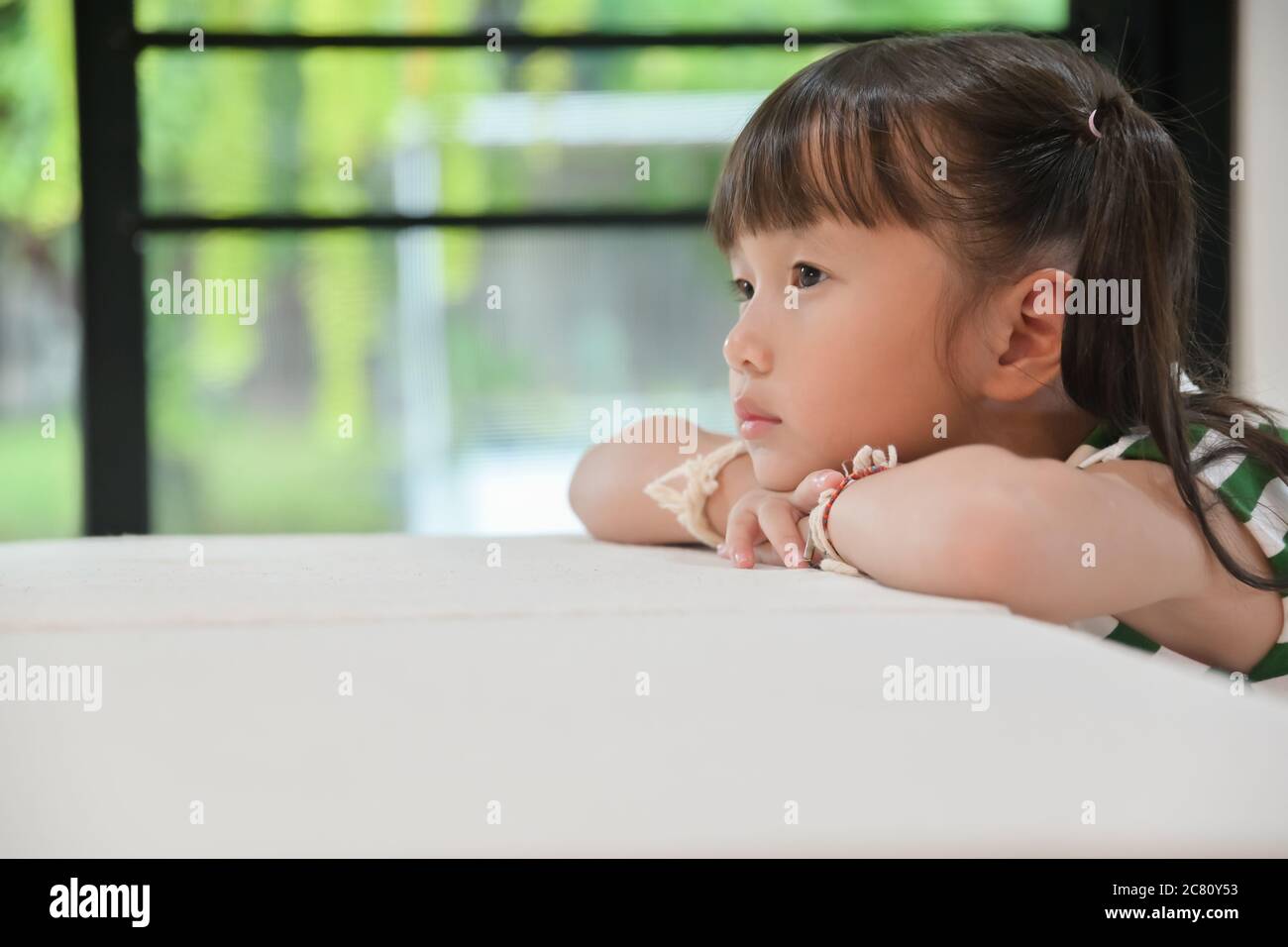 little girl sitting vacant on table feeling empty living without meaning looking forward to no point ,she sad brooded over the bullying done to her Stock Photo