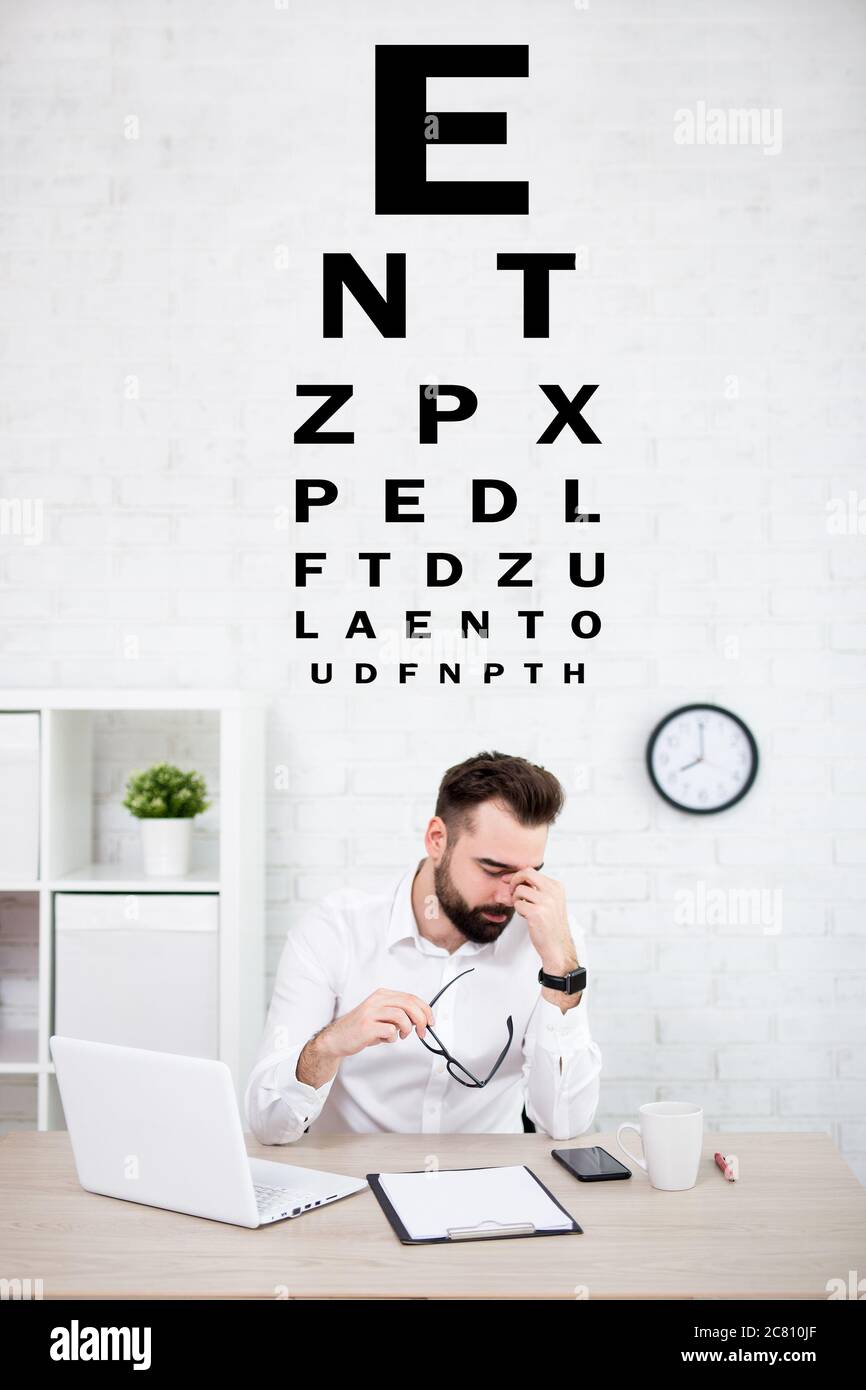 portrait of tired businessman holding eyeglasses and eye test chart in
