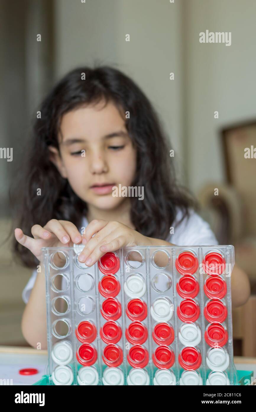 She playing with boardgame is connect 4. black hair girl playing board game connect 4 red and white Stock Photo