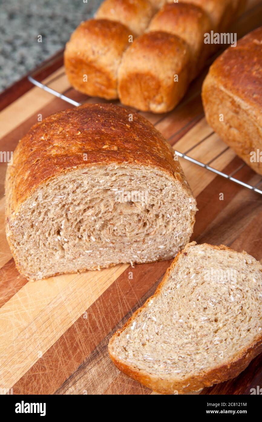 Multigrain rolls and loaf with a slice cut off, on cooling rack and bread board Stock Photo