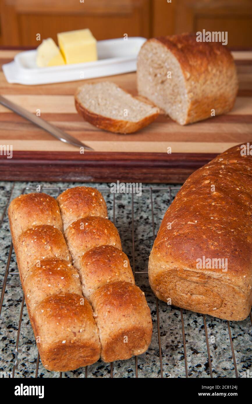 Multigrain rolls and loaf with a slice cut off, with butter and a bread knife Stock Photo