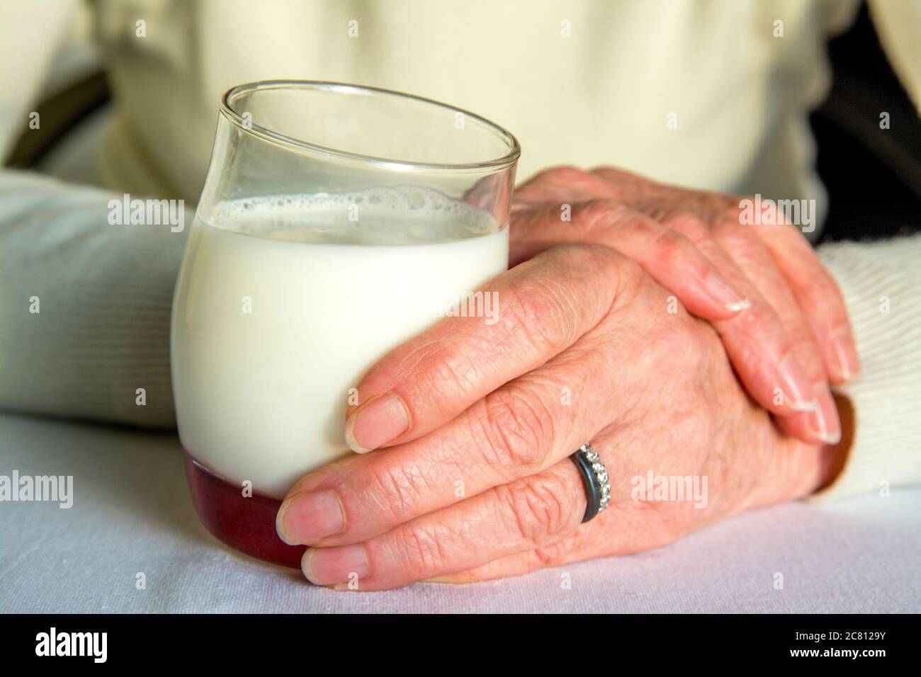 Hands holding a glass of creamy milk with a hint of fruitiness on a soft surface in a serene setting Stock Photo