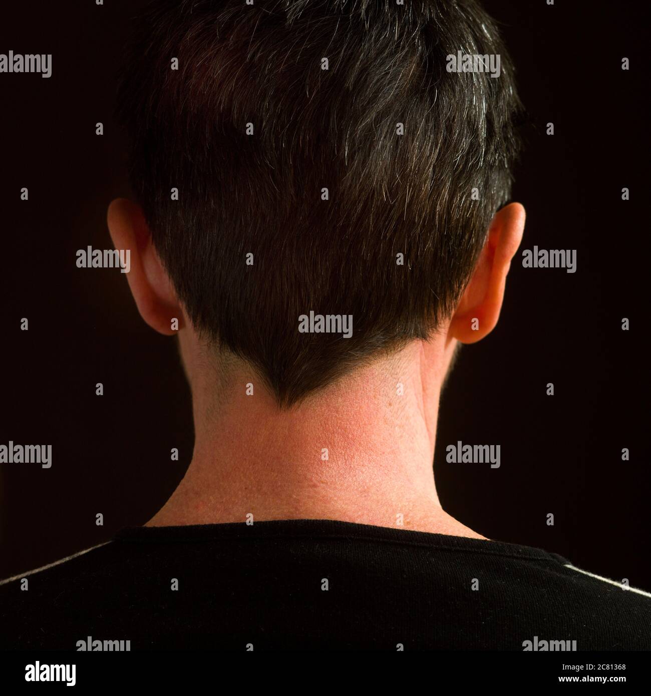 Person with short hair viewed from the back in a dark setting enhancing the elegance of the silhouette Stock Photo